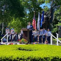 a man stands at a podium in Gale Park with service flags and the statue in the background