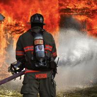 A fire fighter stands in front of a burning home spraying it with water