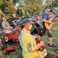 A band performing outside with guitars drums and keyboards