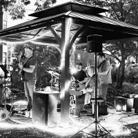 Black and white picture of a group of people playing instruments such as guitar, drums and keyboard