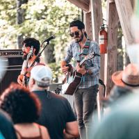 Two people singing and playing guitar outside