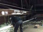 a man leans over the old insulation inspecting it with a flash light