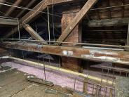 a large wooden beam holds up the roof of the town hall with new pink insulation on the floor