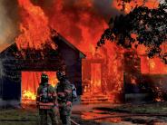 Two fire fighters stand in front of a house that is burning