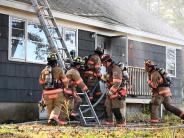 fire fighters outside of a burning home climb a ladder