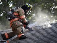 a fire fighter cuts through the roof of a burning home