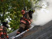 A firefighter uses a saw to cut through the roof of a burning house