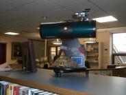 Telescope on top of bookshelf with tortoise beside it.