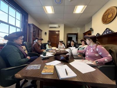 members of the commission wear tricorn hats as they sit around a table planning events and other 250 celebration items