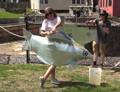 Renay Allen wearing a silver fish mascot costume while holding a real river herring at the 2022 Alewife Festival