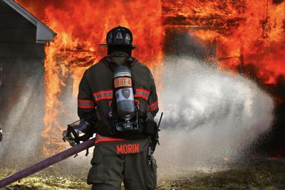 A fire fighter stands in front of a burning home spraying it with water