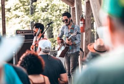 Two people singing and playing guitar outside