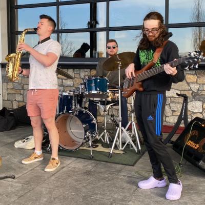 a group of 3 people playing saxophone, guitar and drums